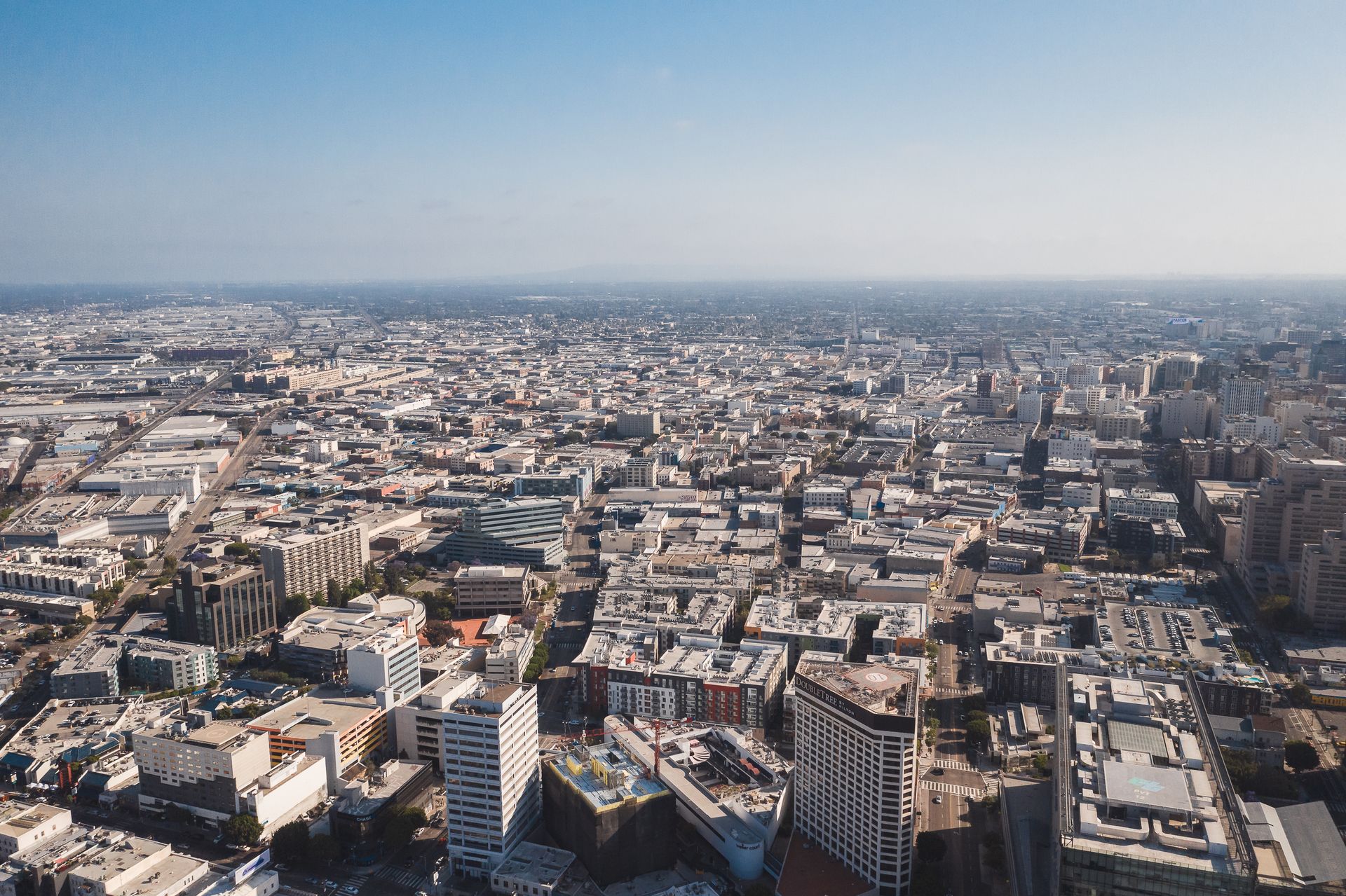 Expansive aerial cityscape of Los Angeles with buildings under a bright blue sky.