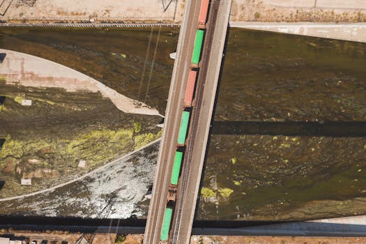 Aerial shot of colorful freight train crossing over a bridge above a river.