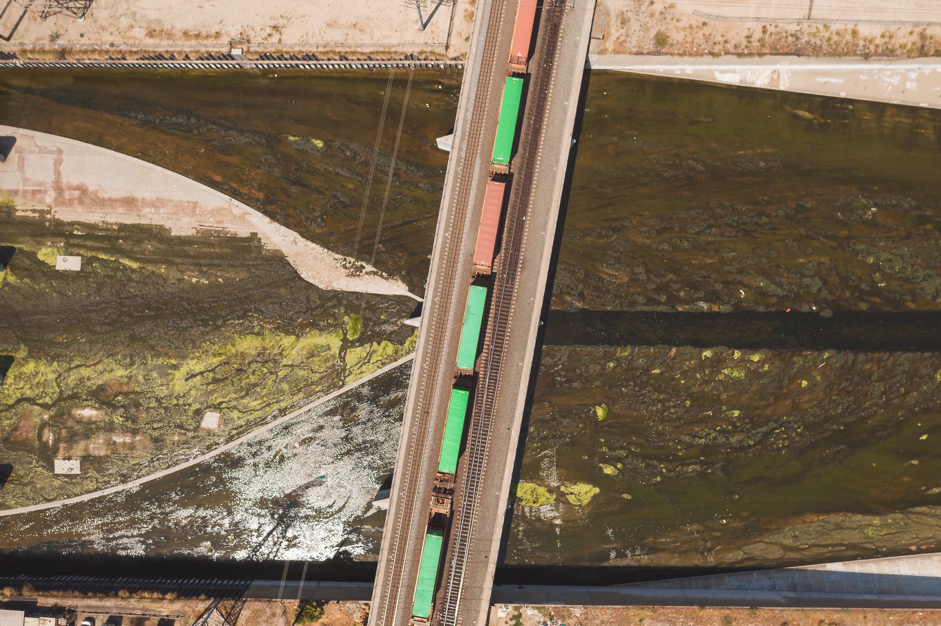 Aerial shot of colorful freight train crossing over a bridge above a river.