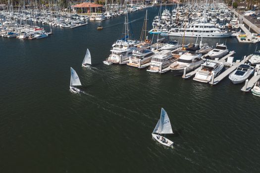 A stunning aerial view of sailboats and yachts in a marina under sunny skies.