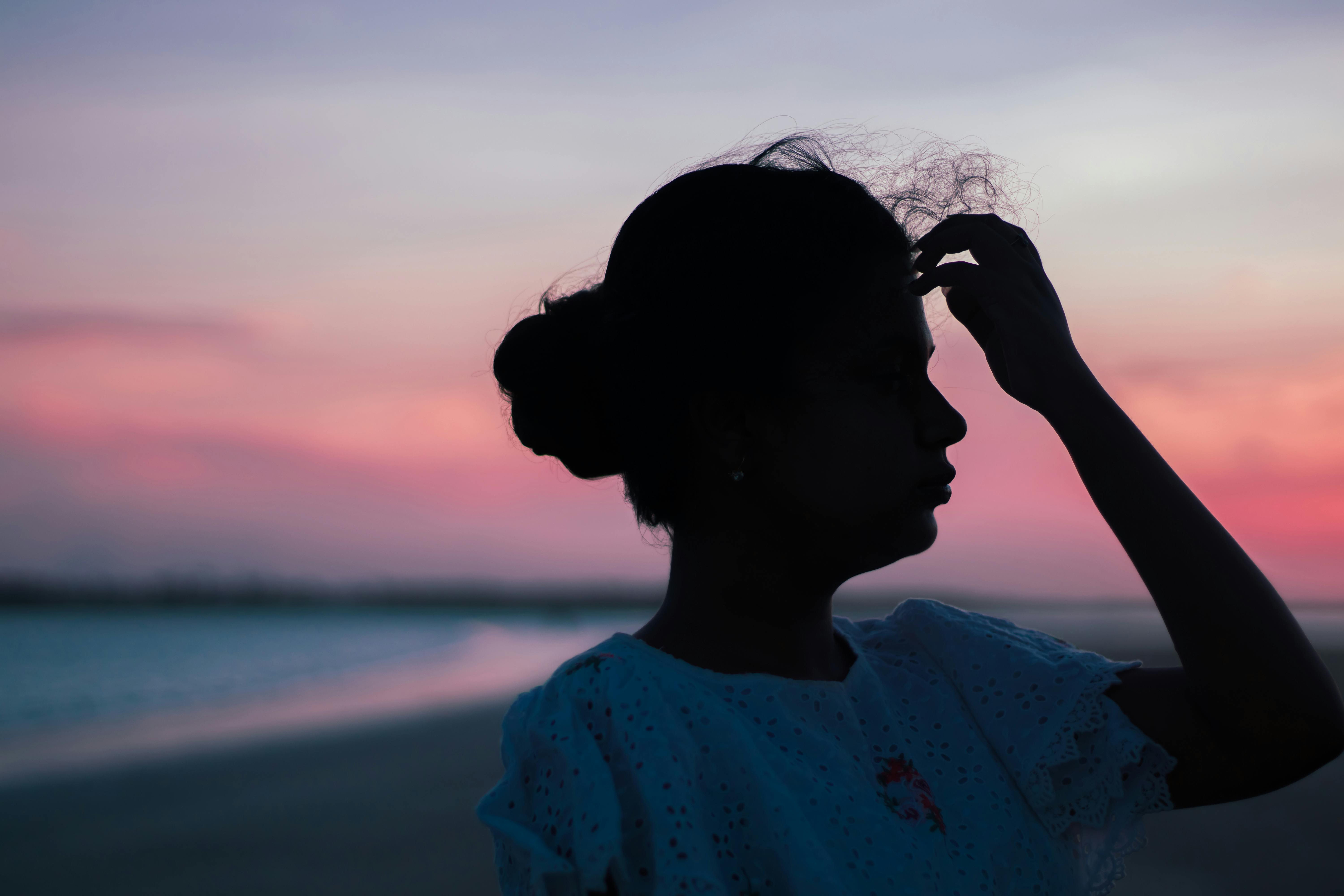 Silhouette of a woman touching her hair against a stunning beach sunset backdrop.