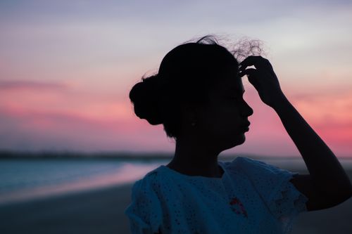 Free Silhouette of a woman touching her hair against a stunning beach sunset backdrop. Stock Photo