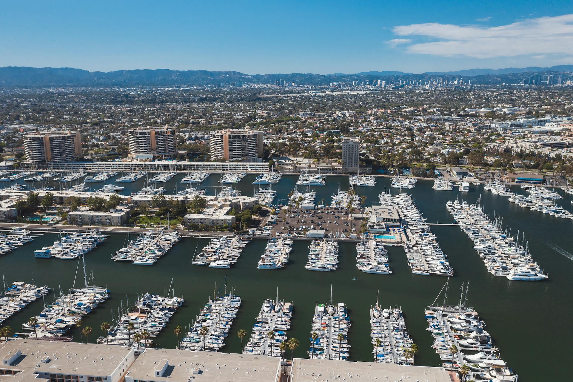 Explore the bustling Marina del Rey Harbor with yachts and cityscape in the background.