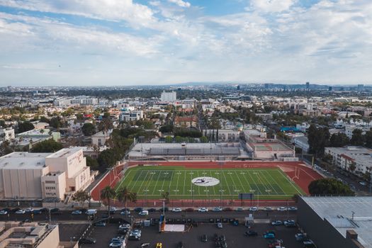 Drone shot capturing an urban football stadium and surrounding cityscape under a bright sky.