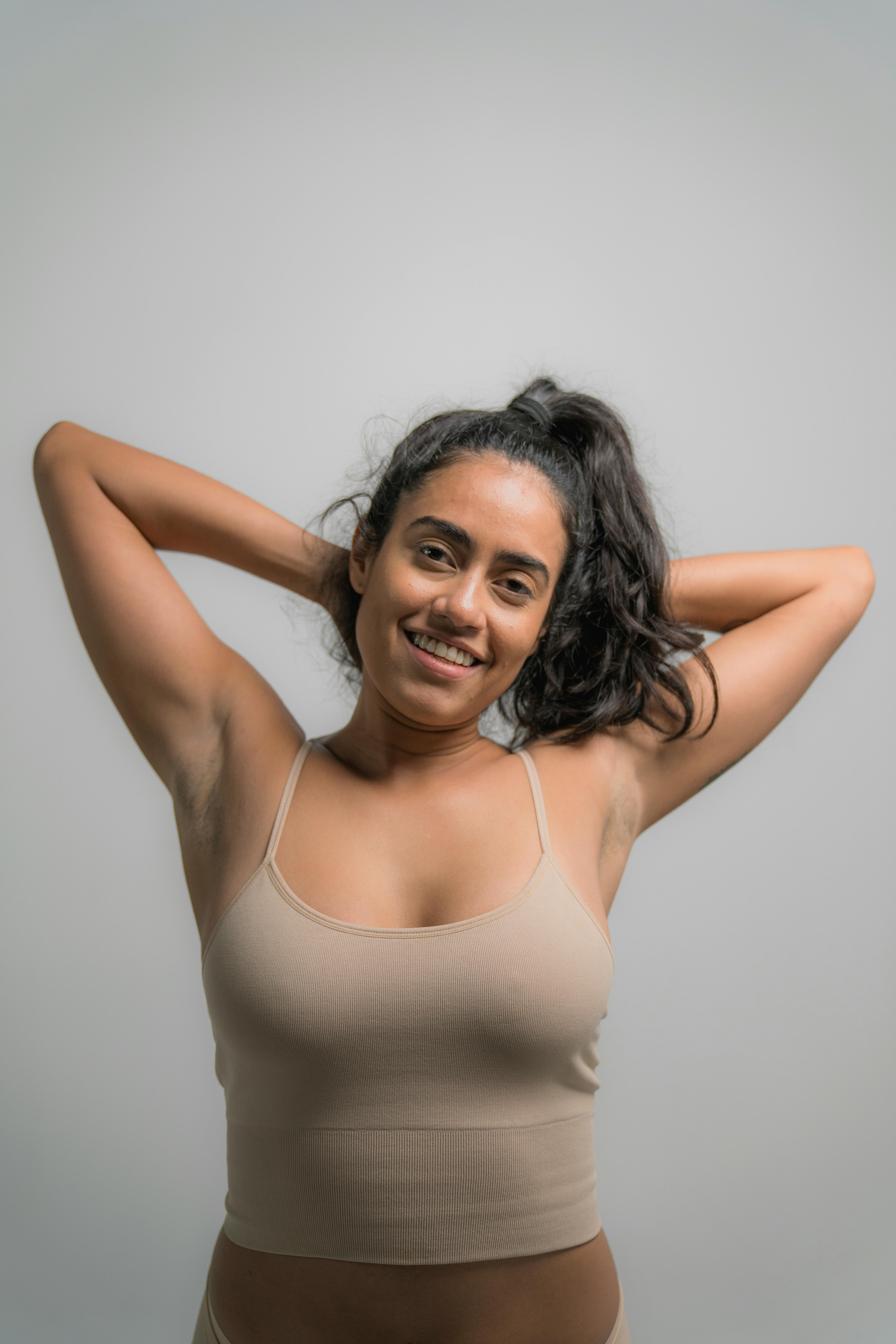 Smiling Hispanic woman in a nude tank top embracing body positivity and confidence.