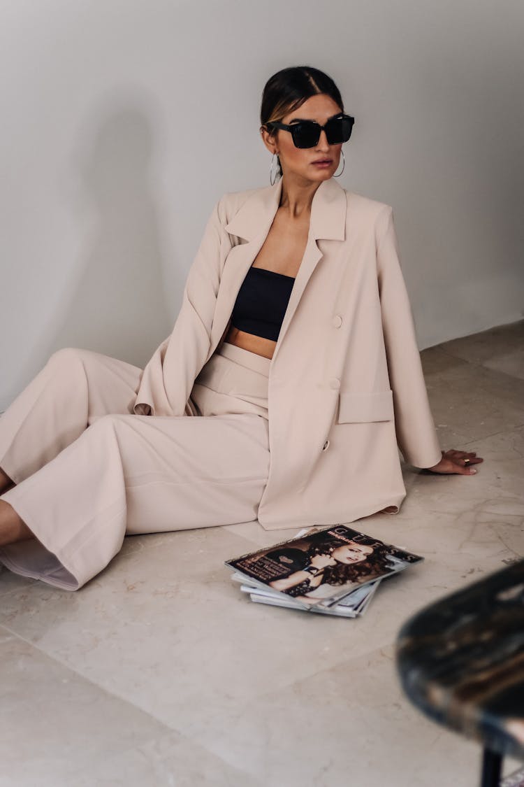 Woman In Beige Blazer And Pants Sitting On The Floor Near Stack Of Magazines