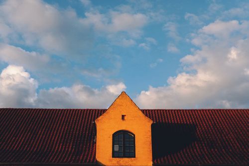 Free Charming attic window and sloped red roof against blue cloudy sky. Stock Photo