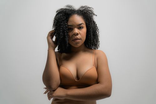 Free Confident woman with curly hair posing in a brassiere against a neutral background. Stock Photo