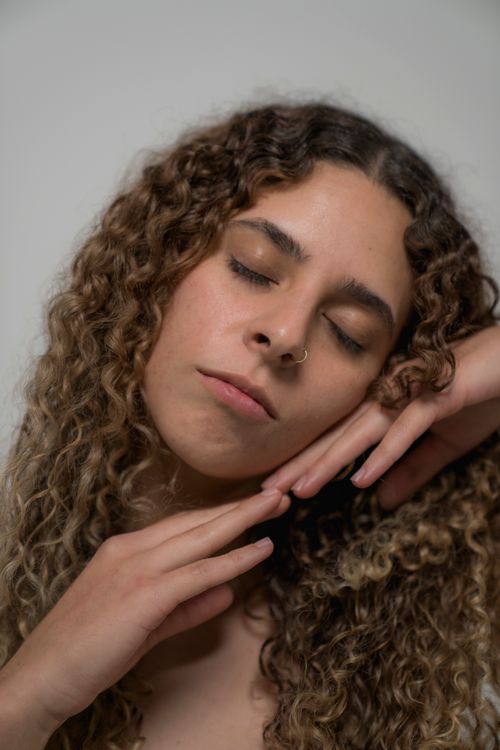 Free Captivating portrait of a woman with curly hair and eyes closed, exuding serene beauty. Stock Photo