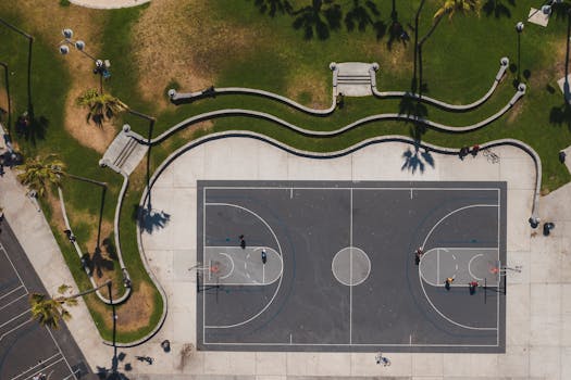 Aerial shot of a basketball court in a sunny park with surrounding greenery.