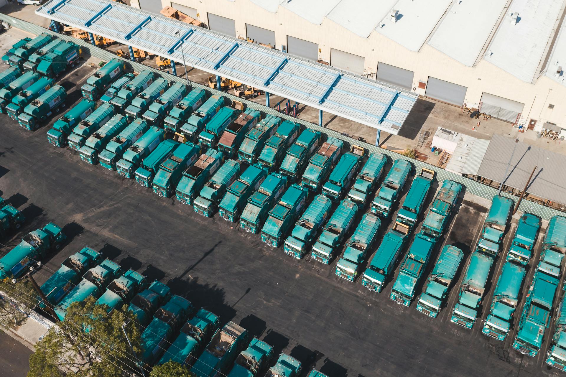 Aerial view of teal trucks lined up in a large industrial parking area next to a warehouse.