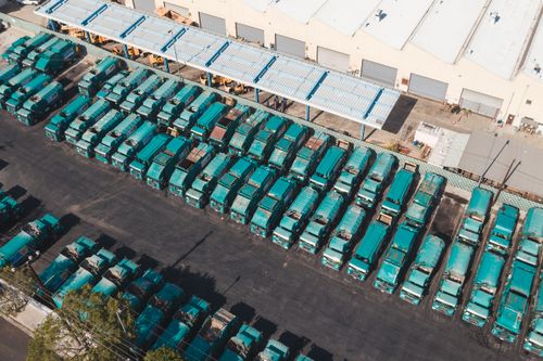 Free Aerial view of teal trucks lined up in a large industrial parking area next to a warehouse. Stock Photo