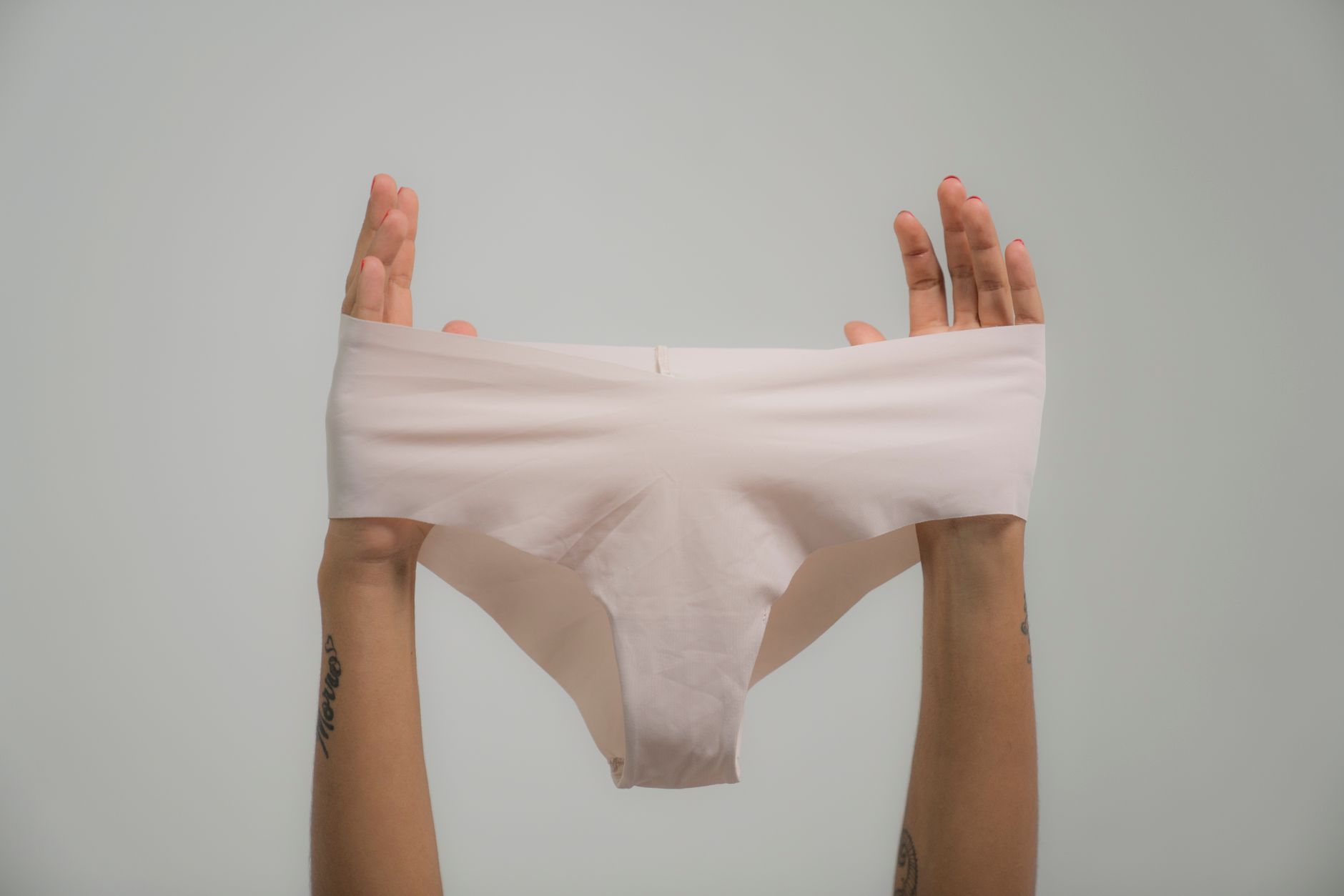 Close-up of hands holding white underwear against a subtle background.