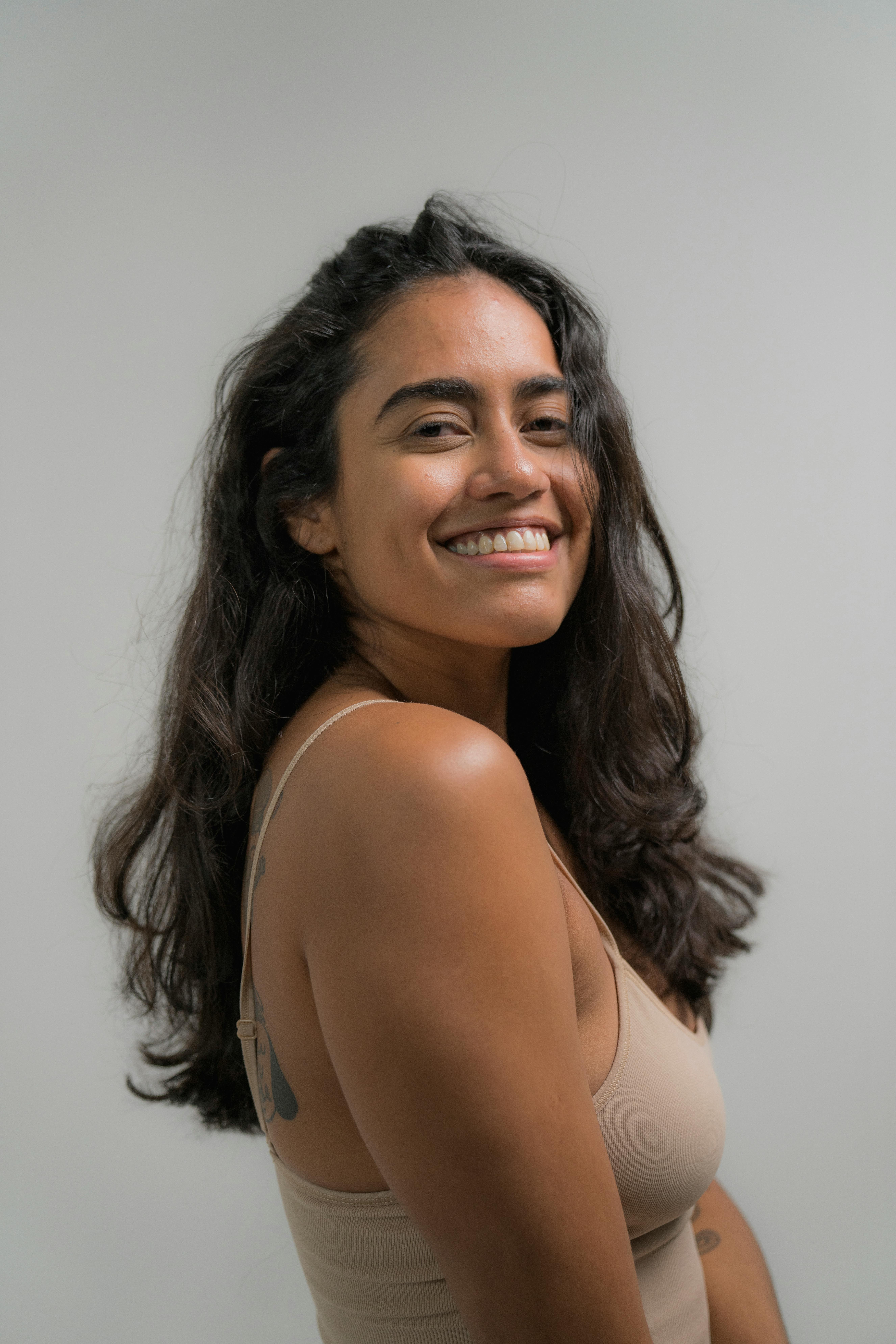 Portrait of a young Hispanic woman with long hair smiling confidently in a neutral studio setting.