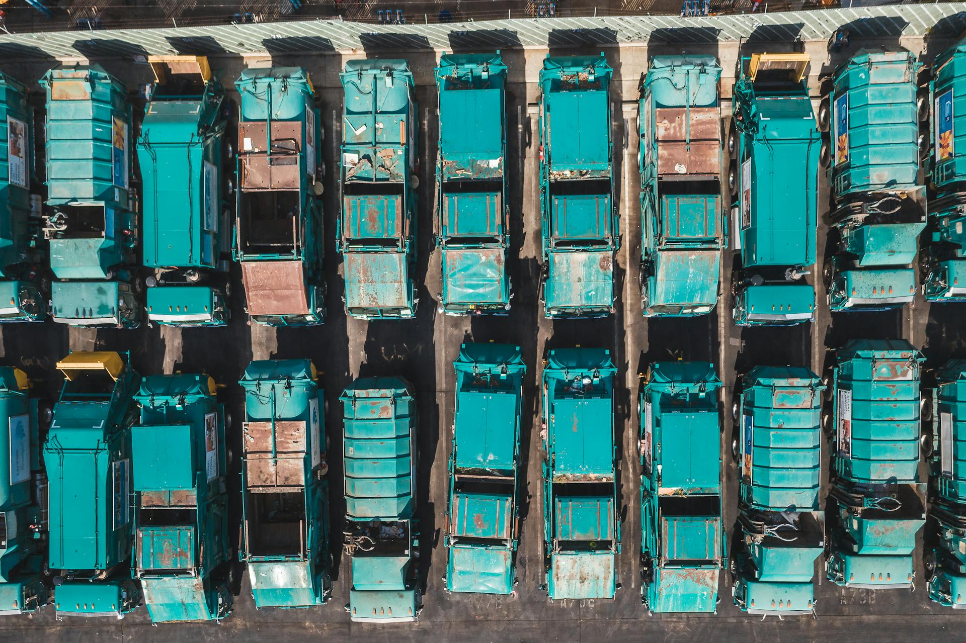 Aerial shot of turquoise garbage trucks parked in neat rows, showcasing a pattern of urban utility vehicles.