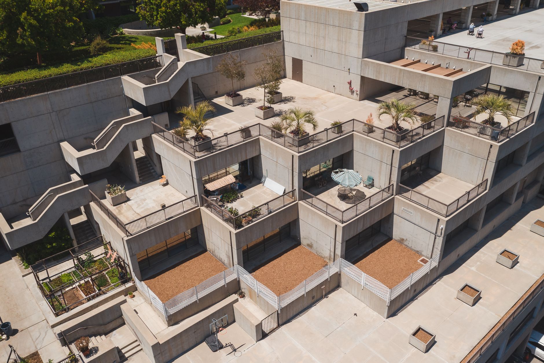Aerial view of a modern urban building showcasing concrete terraces with greenery and geometric design.