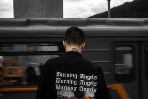 Free Man in a 'Burning Angels' jacket standing by a moving train in an urban setting. Stock Photo