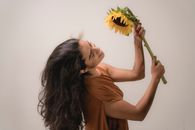 A joyful woman in a brown dress smiling and holding a large sunflower.