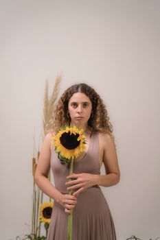A woman poses indoors with a bright sunflower, capturing a minimalist and warm aesthetic.