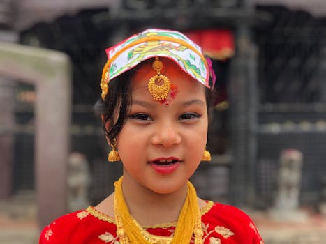 A young girl in vibrant traditional Nepali attire and jewelry, outdoors in Madhyapur Thimi.