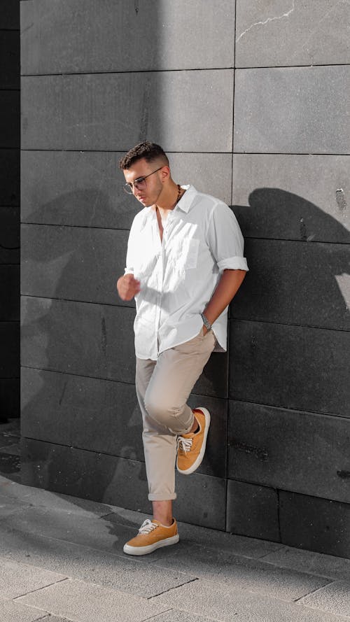 Download A Young Man In A White Shirt Leaning Against A Wall