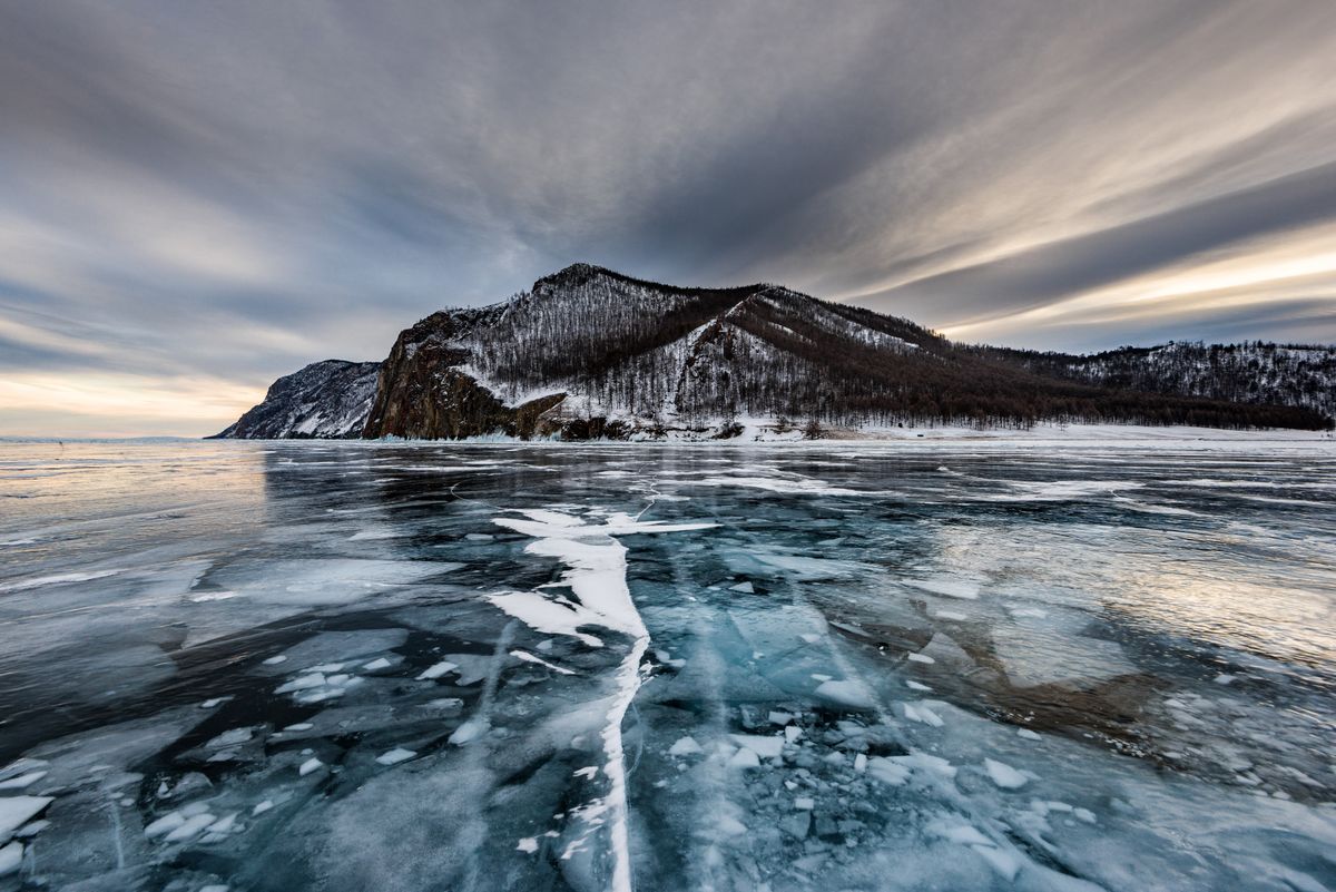 Stunning view of frozen Lake Baikal during winter with dramatic skies and snow-covered mountains.