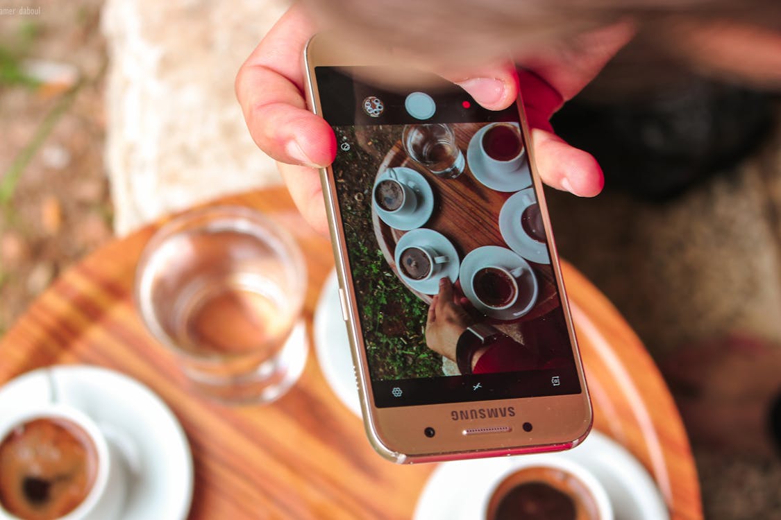 Free Person Holding a Samsung Galaxy Smartphone Taking a Picture on Their Coffees Stock Photo