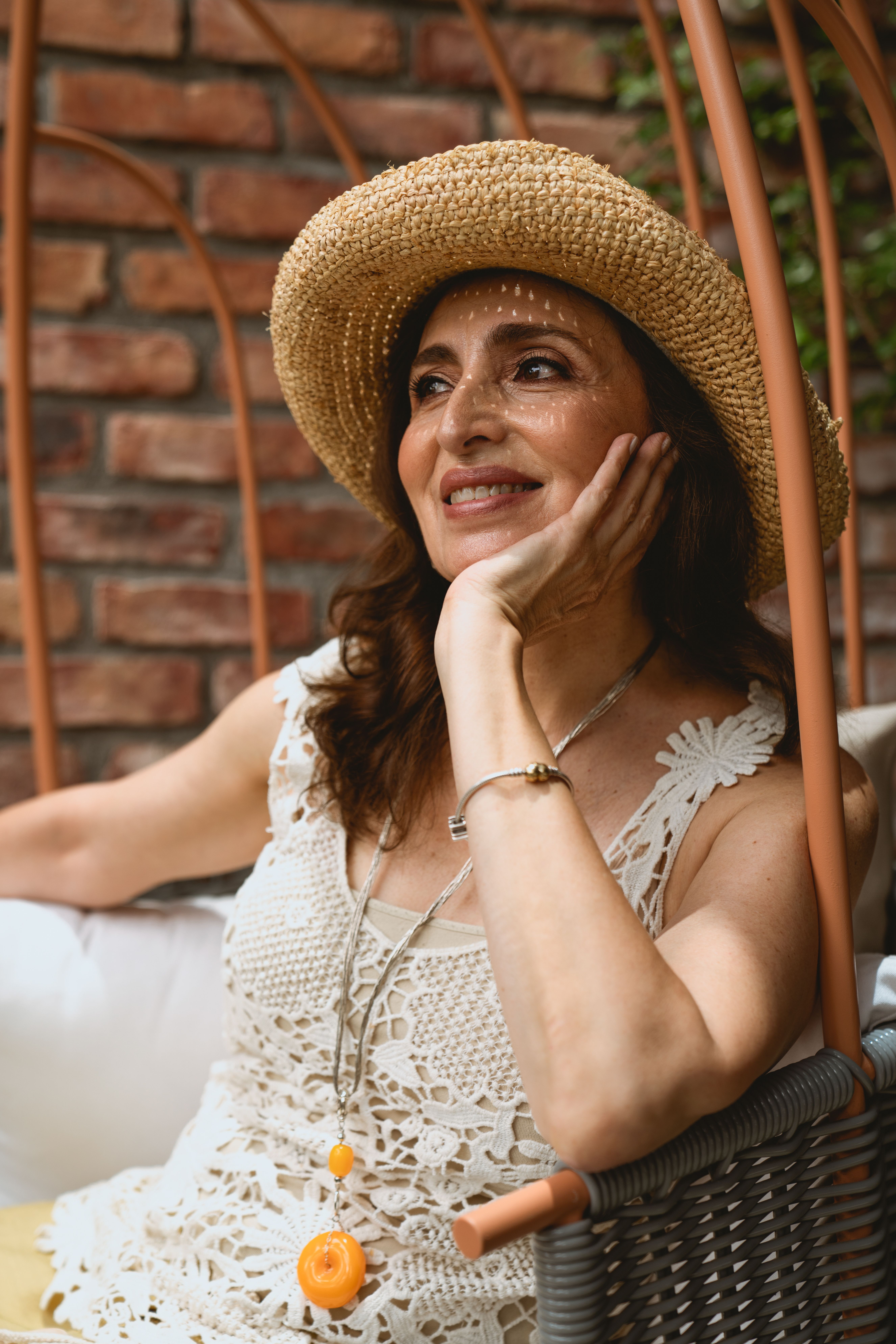 Charming senior woman in straw hat and lace top sitting and smiling outdoors. Relaxing summer vibe.