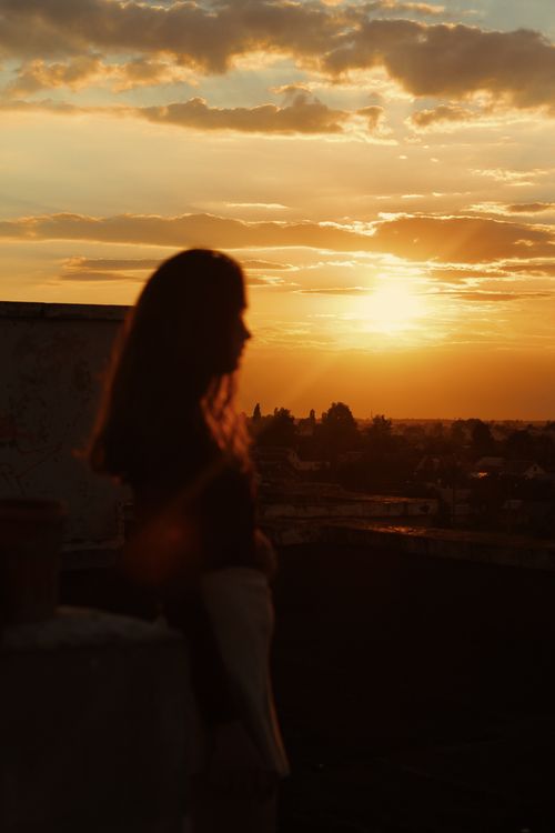 Free A silhouette of a woman on a rooftop with a vibrant sunset background, creating a dramatic scene. Stock Photo