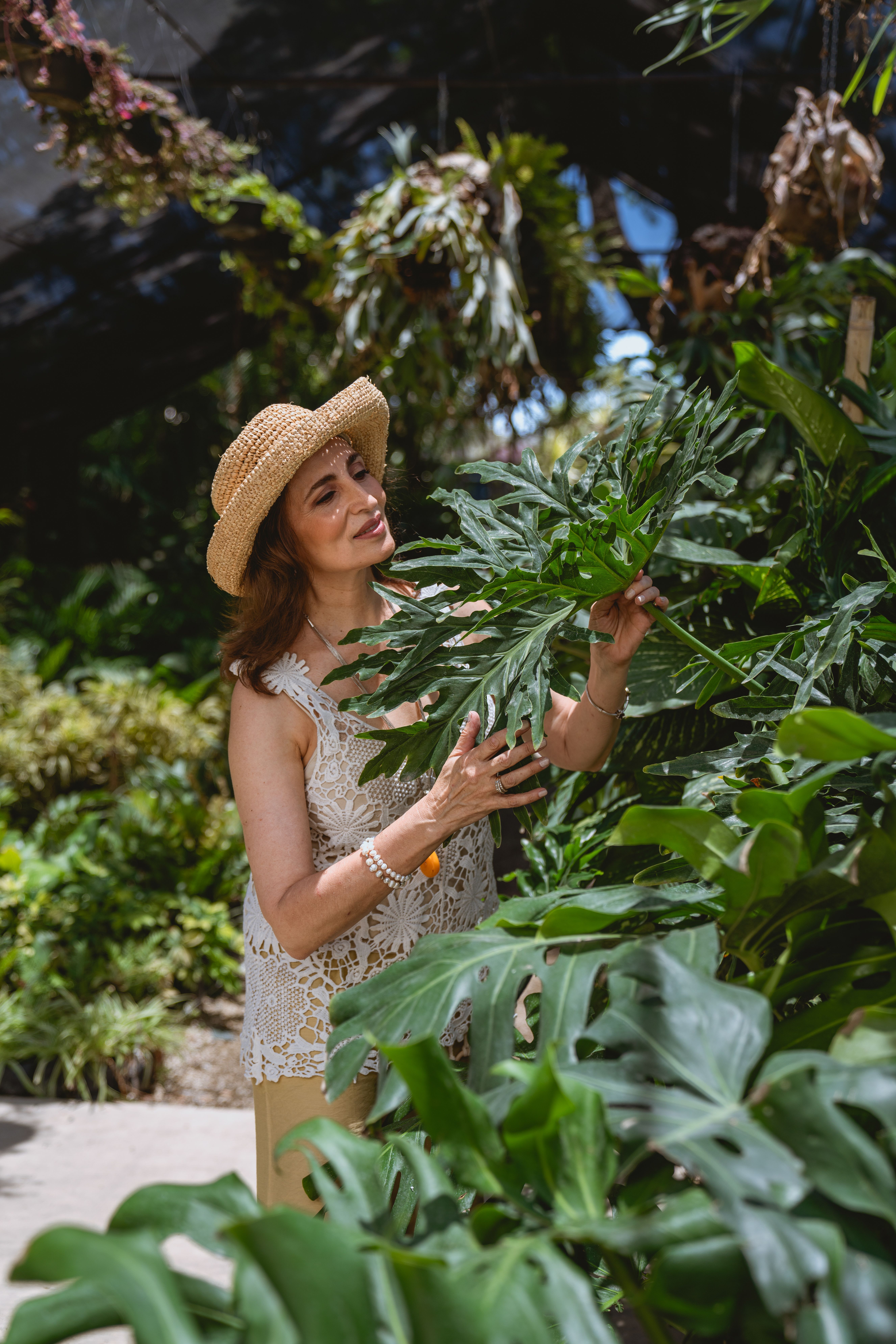 Senior woman in a lace top and hat exploring lush greenery in a botanical garden.