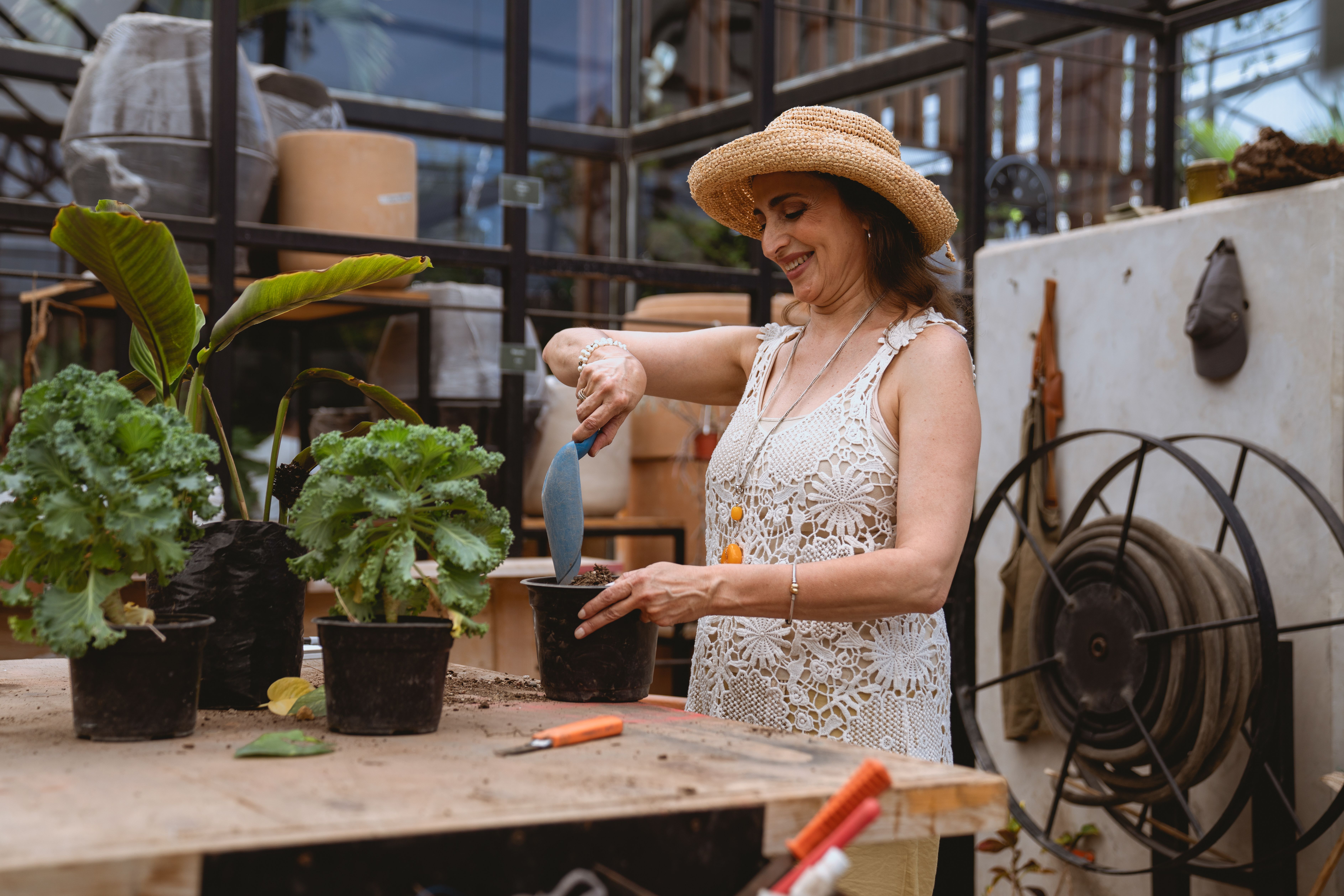 Smiling woman in a straw hat gardening indoors with potted plants.