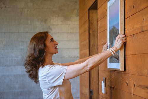 A Woman Hanging a Frame on Wooden Wall