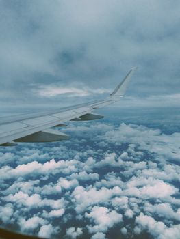 View of clouds from an airplane window with a visible wing in a cloudy sky.