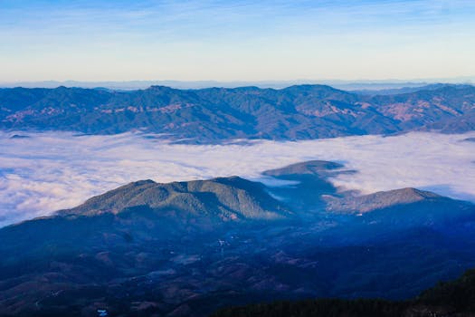 Captivating view of mountains draped in clouds with clear blue skies above, showcasing nature's serene beauty.