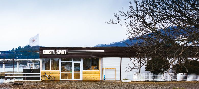 Khosta Spot café in Sochi, Russia, featuring a bicycle, bare trees, and a flag in a serene setting.