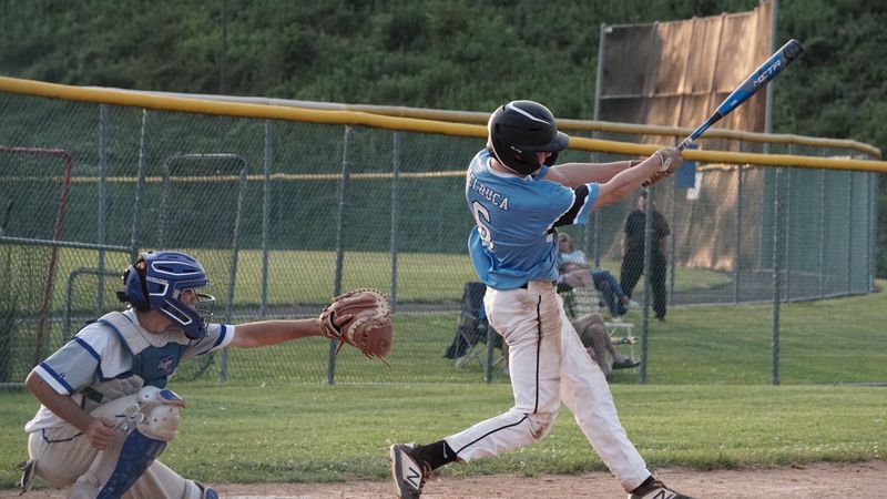 Youth baseball player swings the bat during a game on a sunny day.