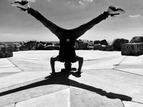 A man performing a headstand outdoor with a striking shadow cast on the ground.