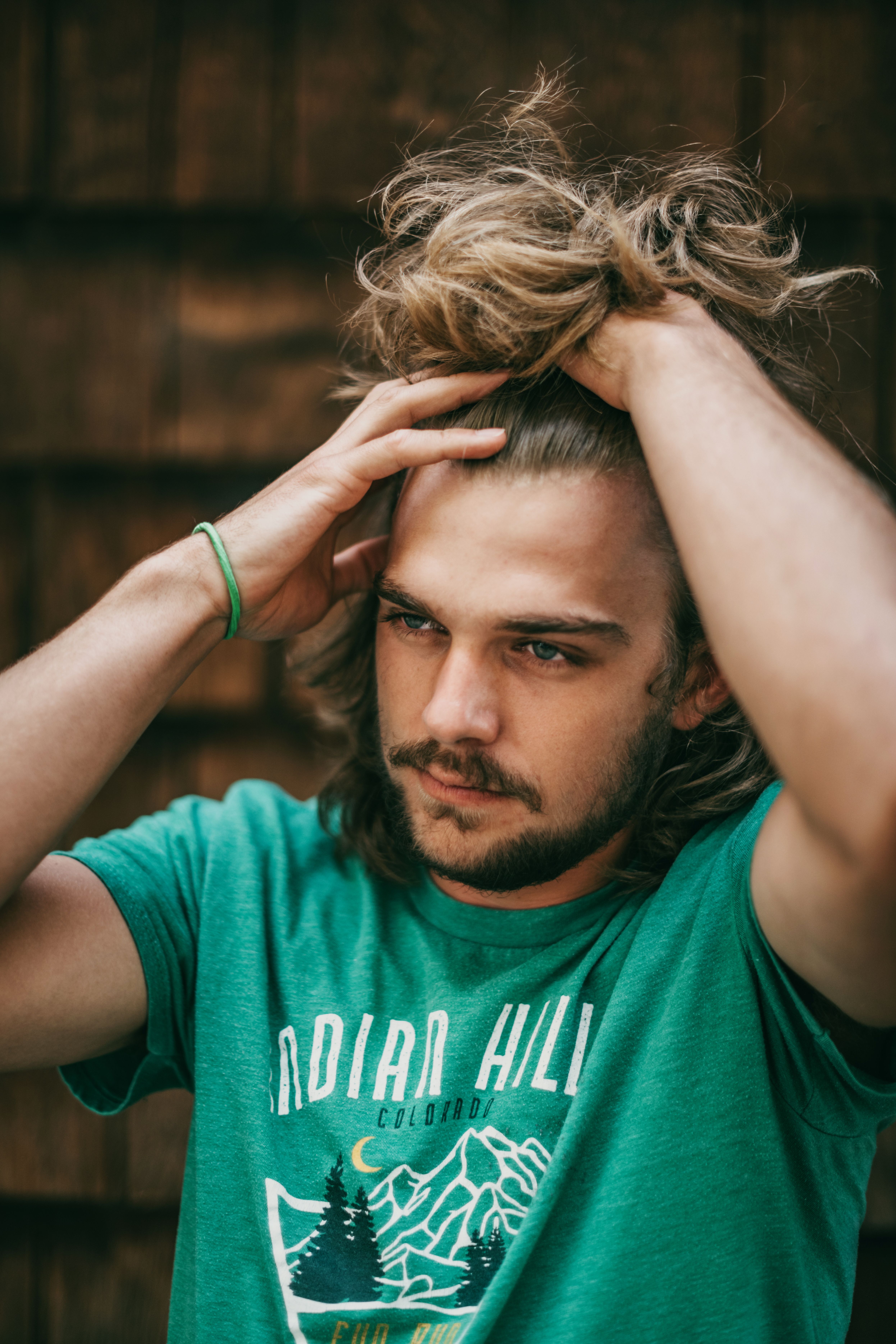 Casual portrait of a young man holding his hair, wearing a green shirt outdoors.