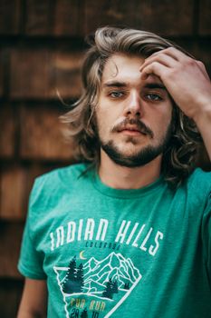 Close-up portrait of a young bearded man with long hair outdoors.