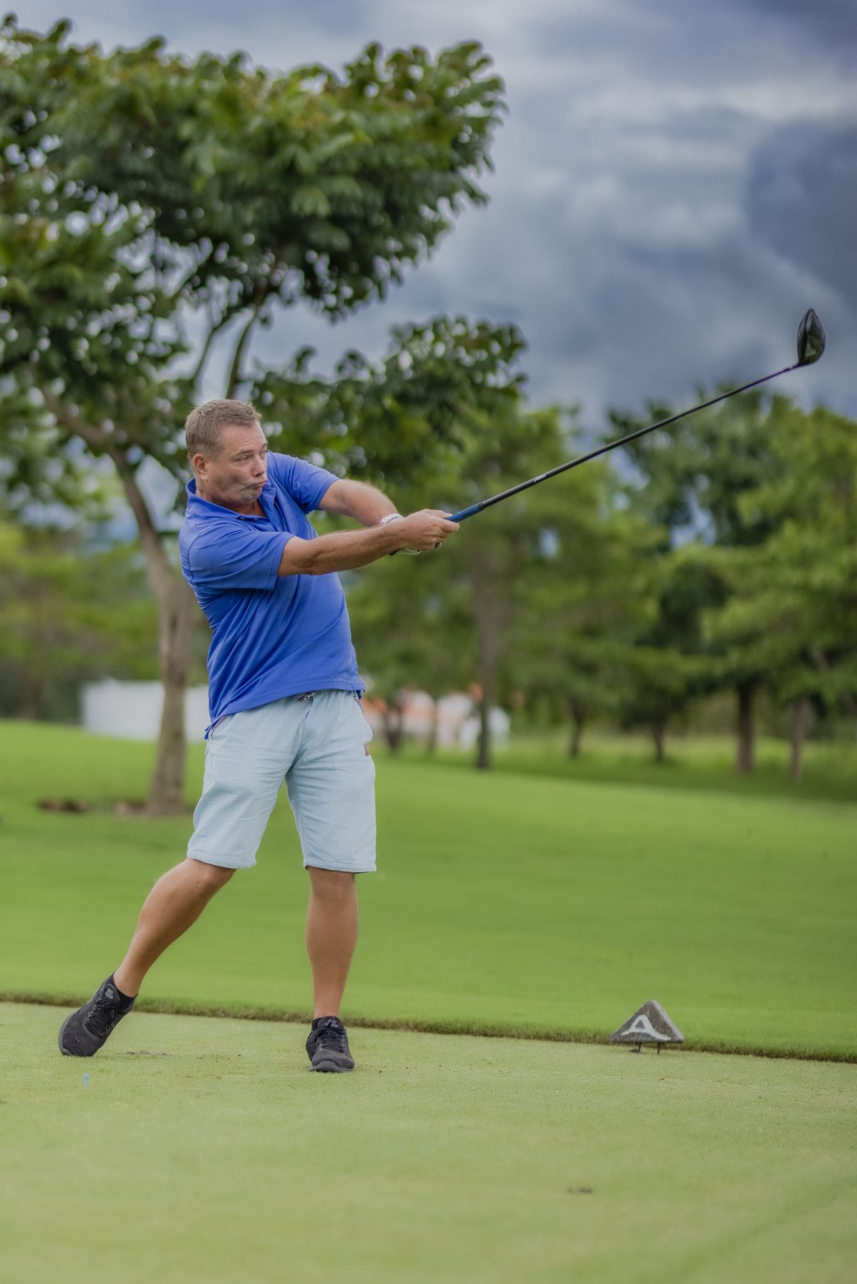 Male golfer wearing a blue performance polo and light shorts during a full golf swing