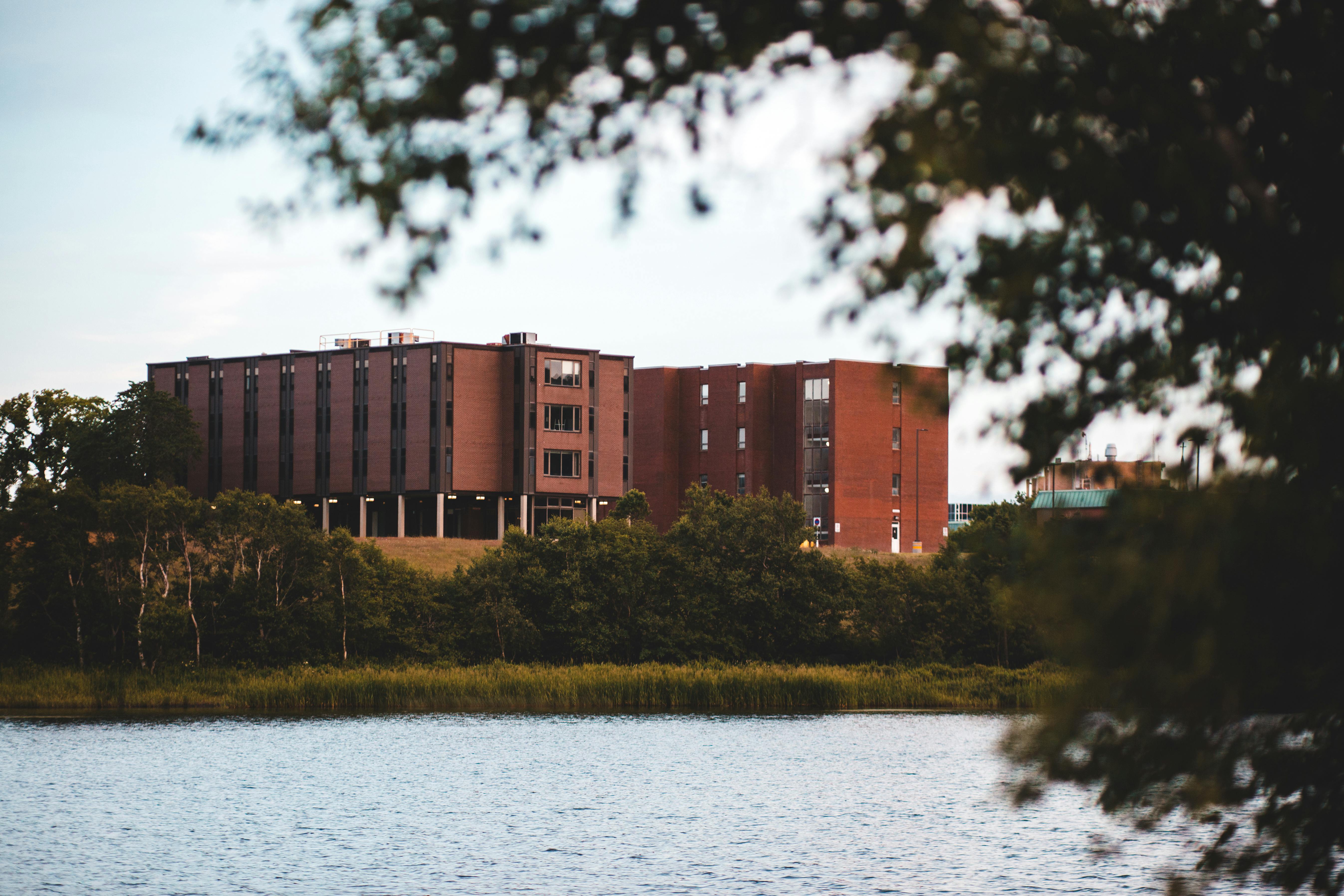 A modern brick building surrounded by trees near a serene lake, captured during the day.