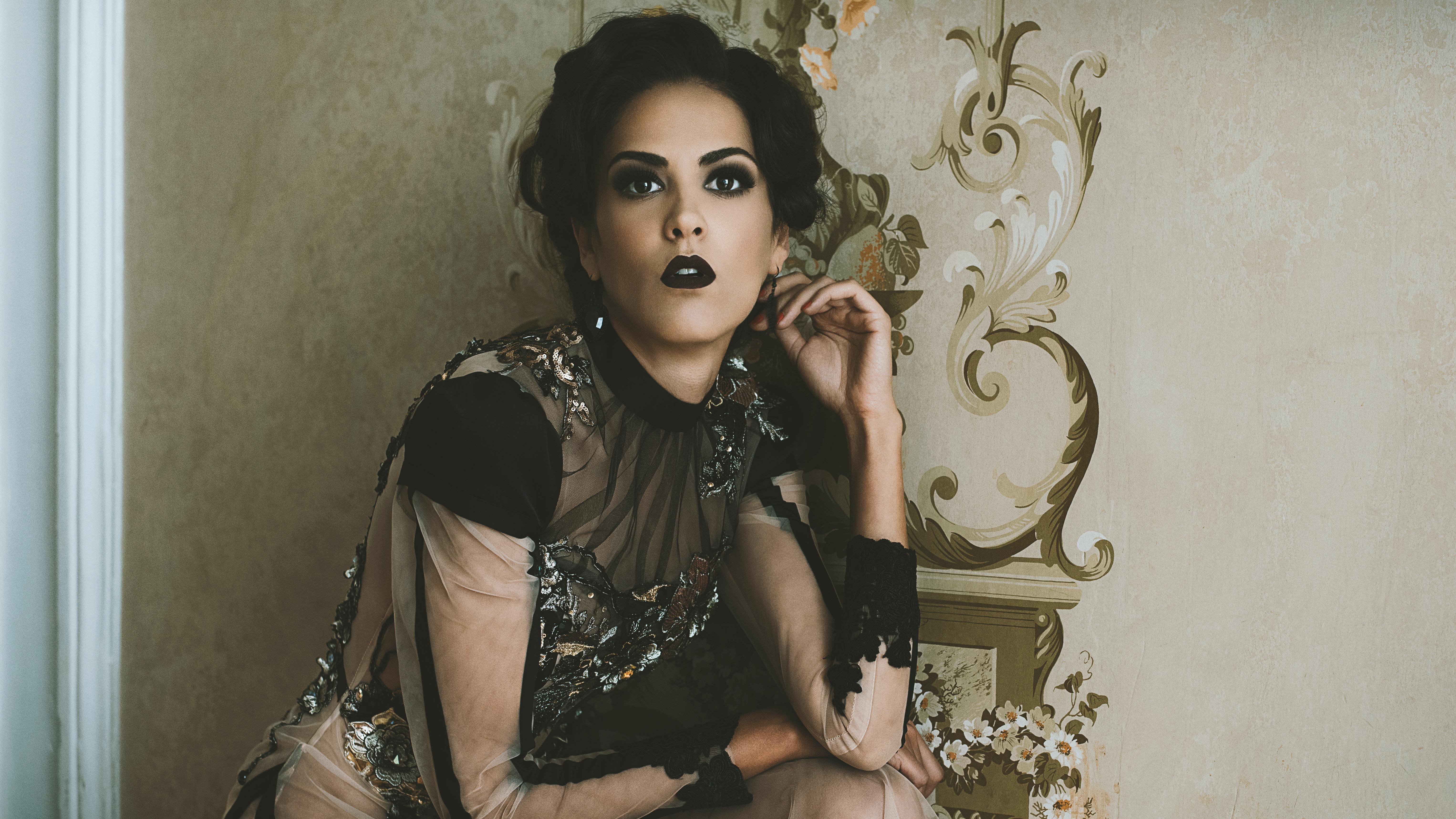 Sophisticated portrait of a woman with bold black lipstick, styled in glamour fashion, set against an ornate wallpaper.