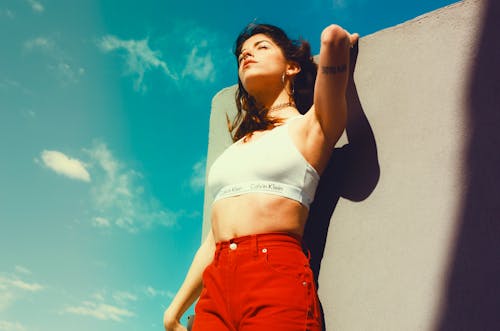 흰색 캘빈 클라인 스포츠 브래지어와 회색 하늘 아래 회색 벽에 기대어 빨간 바지에 여자