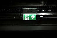 在黑暗的工业环境中，明亮的绿色紧急出口标志带有箭头，指示疏散路线