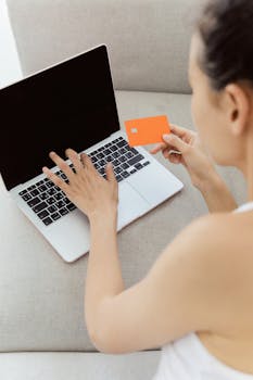 Woman holding credit card making online purchase on laptop computer, representing e-commerce.