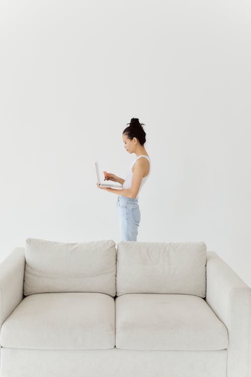 Woman Standing Behind Gray Couch Using Laptop