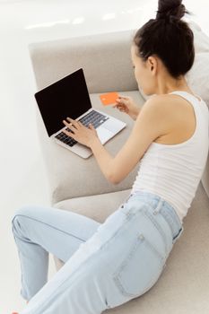 Young woman using a laptop and credit card for online shopping while lounging on a sofa.