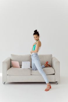 Stylish young woman posing with shopping bags and laptop on a couch indoors.
