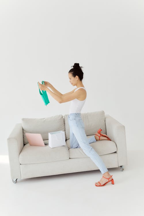 Free Stylish woman examines newly purchased clothes at home, showcasing modern fashion and online shopping. Stock Photo