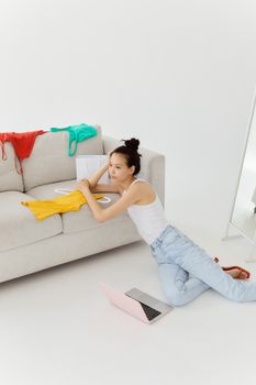 Stylish young woman lounging near a couch with a laptop, showcasing a relaxed lifestyle indoors.